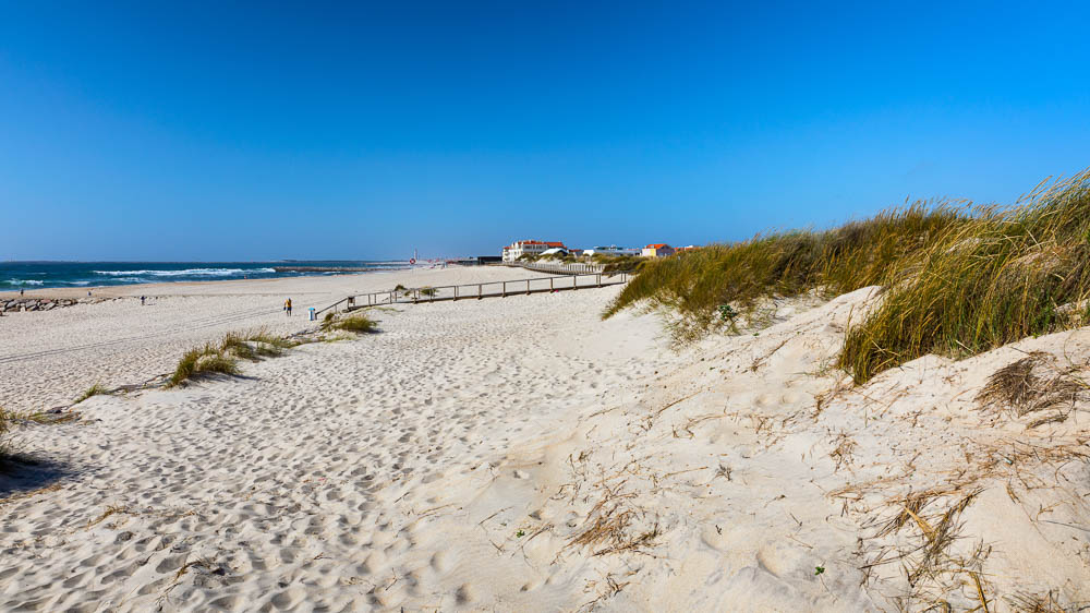 Wooden path at Costa Nova d'Aveiro, Portugal, over sand dunes with ocean view, summer evening. Wooden footbridge of Costa Nova beach in a sunny day. Aveiro, Portugal.